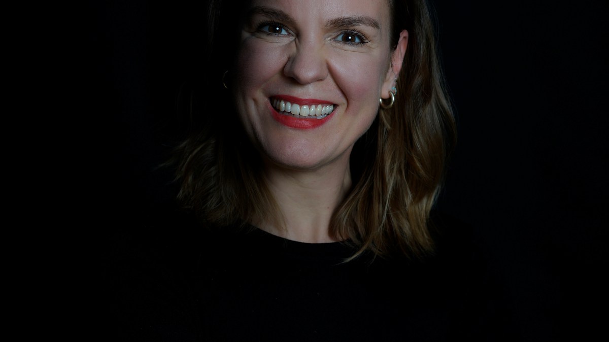 Smiling woman with shoulder-length hair in a dark setting.